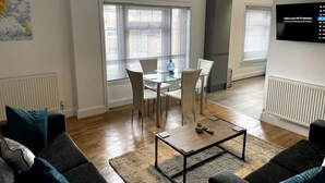 A modern living room with a glass dining table, a sofa, and a TV mounted on the wall. - Spacious Central Apartment (Cheshire East)