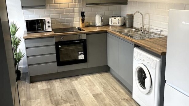 A modern kitchen with a built-in oven, microwave, and washing machine. - Spacious Central Apartment (Cheshire East)