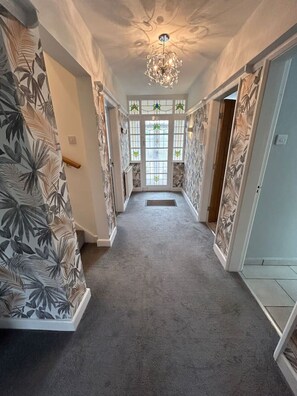 A hallway with patterned wallpaper, a chandelier, and a view through a glass door.