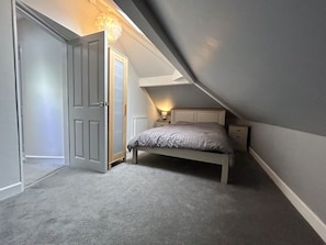A bedroom with a bed, a nightstand, a lamp, and a door. - Fresh and Spacious House (Denbighshire)