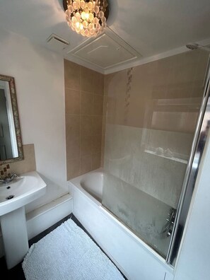 Un baño con lavamanos blanco, bañera, cabina de ducha y lámpara en el techo.