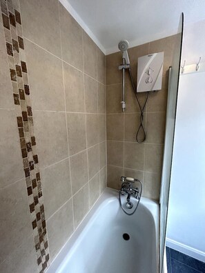 A shower with a handheld showerhead, a wall-mounted control panel, and a bathtub with a faucet.