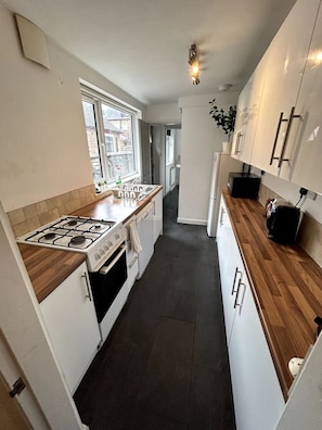 Una cocina estrecha con estufa a gas, armarios blancos, encimera de madera y ventana que proporciona luz natural.