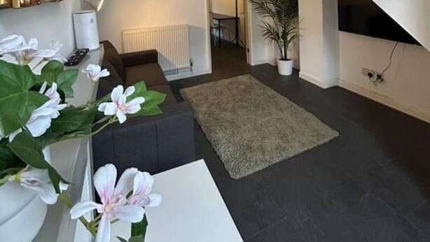 Ein modernes Wohnzimmer mit einer Couch, einem weißen Tisch, einer Topfpflanze und einem großen Spiegel.