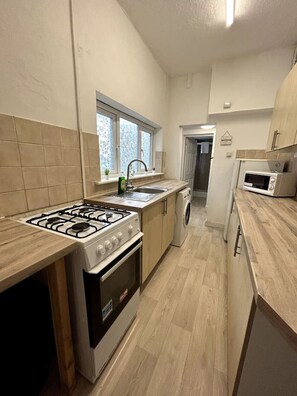 A kitchen with a gas stove, oven, microwave, and a washing machine.