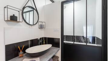 Um banheiro moderno com uma pia oval grande, um espelho e uma porta preta.