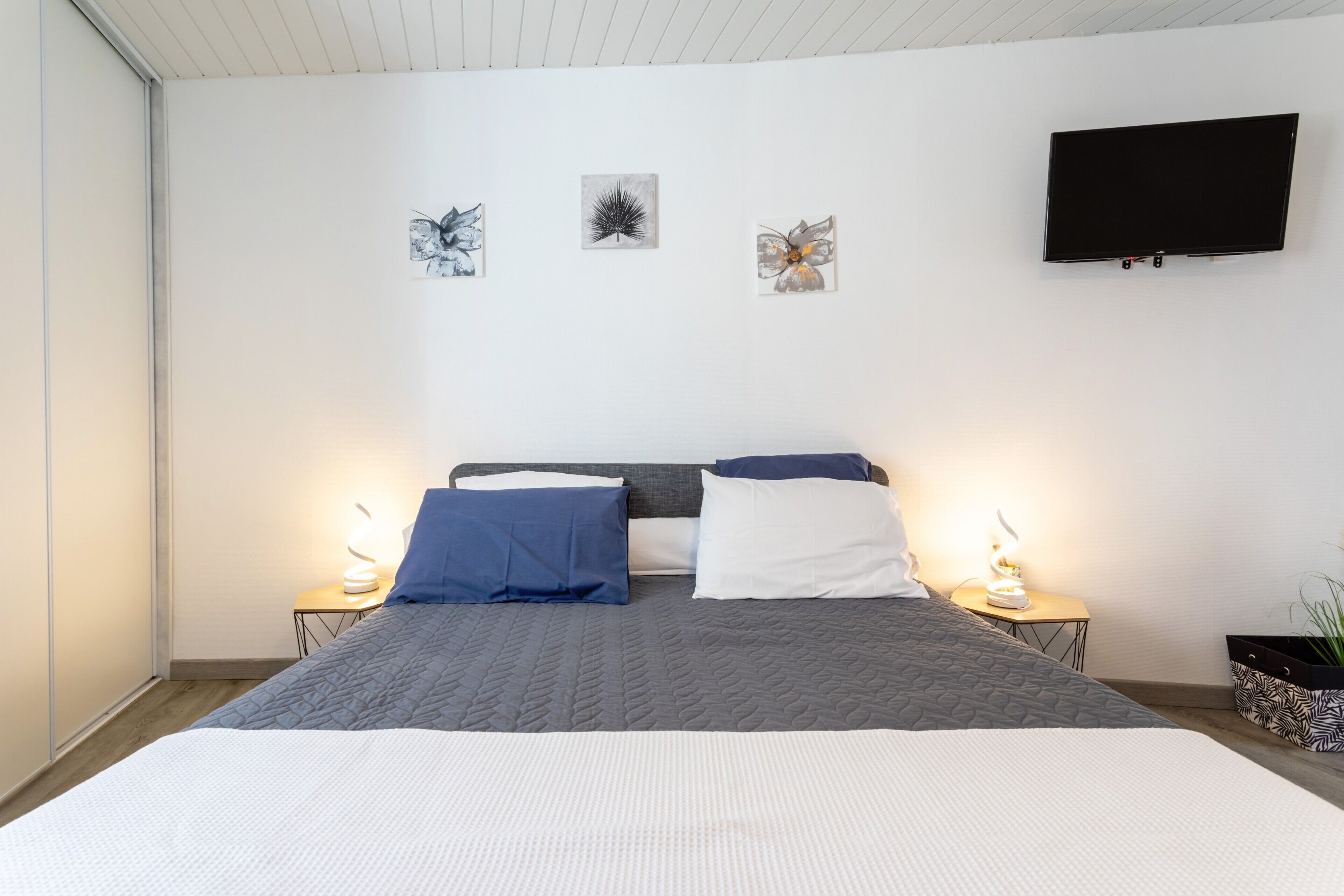 Une chambre à coucher avec un lit, des lampes de chevet, un téléviseur à écran plat et des œuvres d’art accrochées au mur.