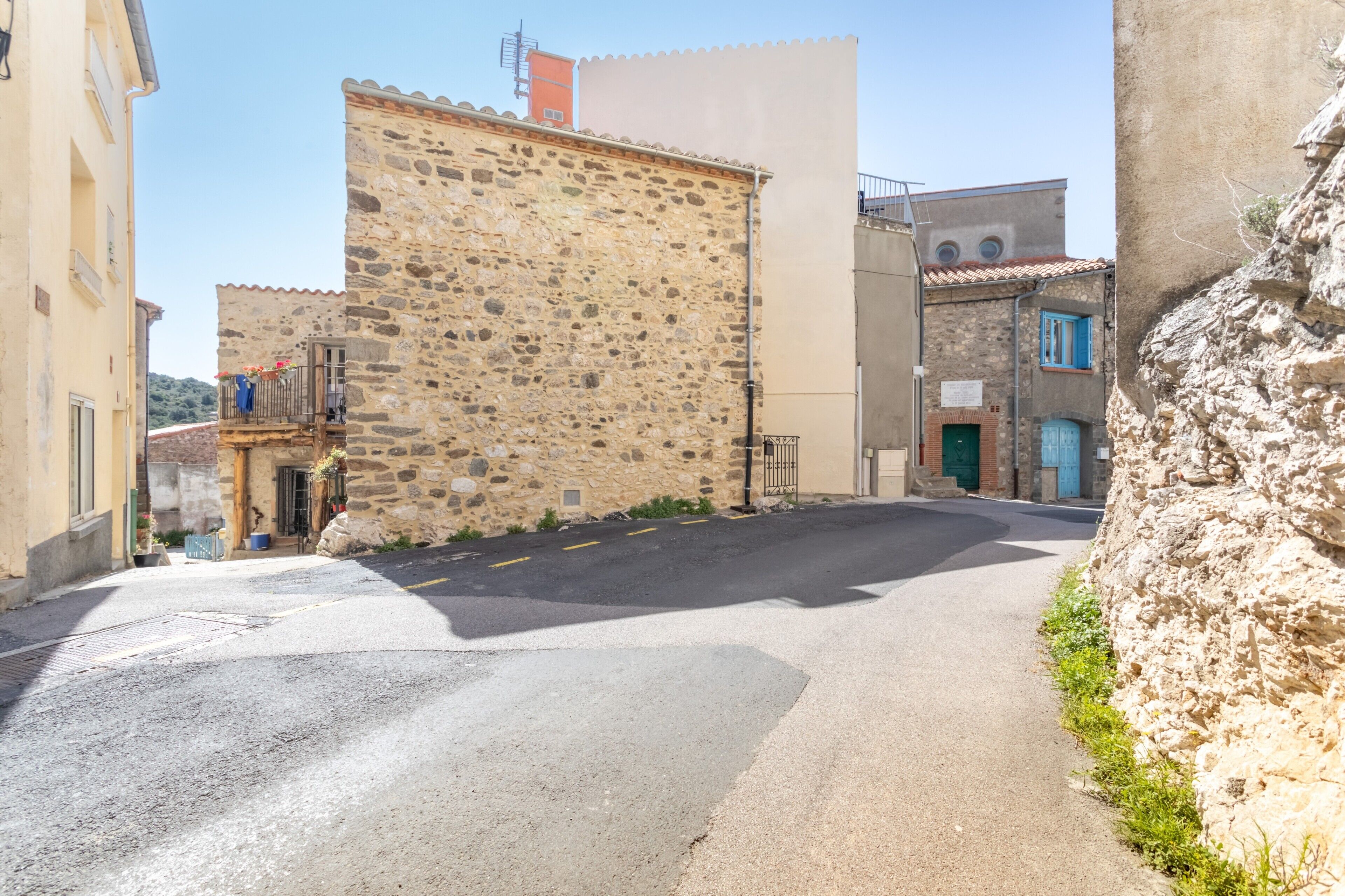 A narrow street with stone buildings, a clear sky, and a visible sign.