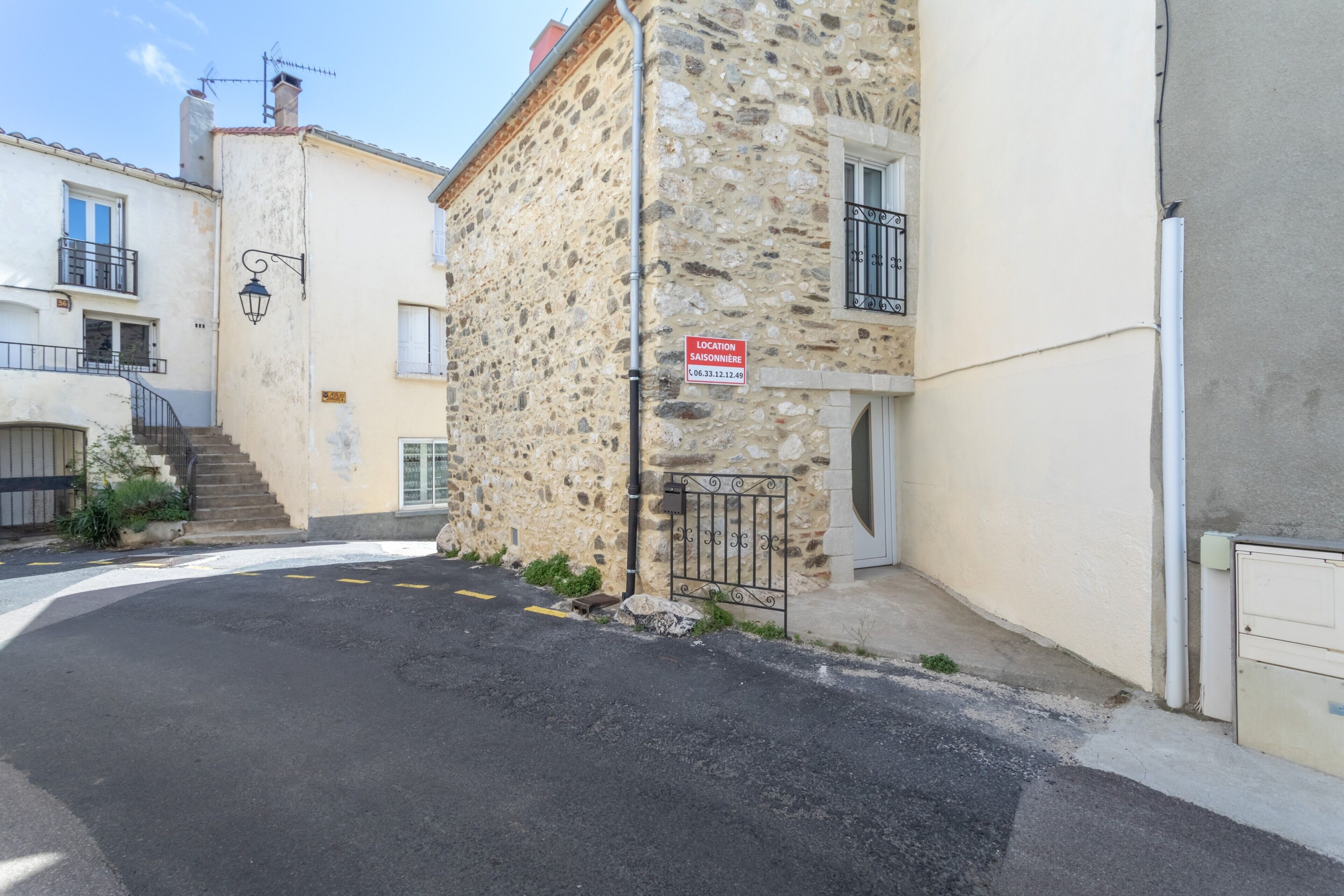 Eine enge Gasse mit Steinbauten, einem Metallgitter und einem Schild, das einen Ort angibt.