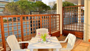 A balcony with a table and chairs, a wooden fence, and a view of a building with blue balconies and trees. - Modern Residence Flat With Balcony-beahost (San Michele al Tagliamento)