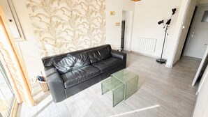 A modern living room with a black leather sofa, a glass coffee table, and a patterned wallpaper. - Renovated House with Garden, Near Beach, Sleeps 4, Pet-Friendly, Private Parking (La Tranche-sur-Mer)