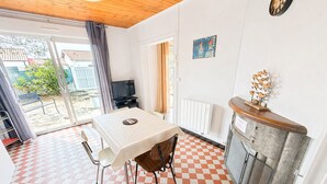 A room with a checkered floor, a table with chairs, a television, a radiator, and a clock on the wall. - Renovated House with Garden, Near Beach, Sleeps 4, Pet-Friendly, Private Parking (La Tranche-sur-Mer)