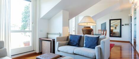 Una sala de estar moderna con un sofá, una lámpara y vistas al exterior a través de amplios ventanales.