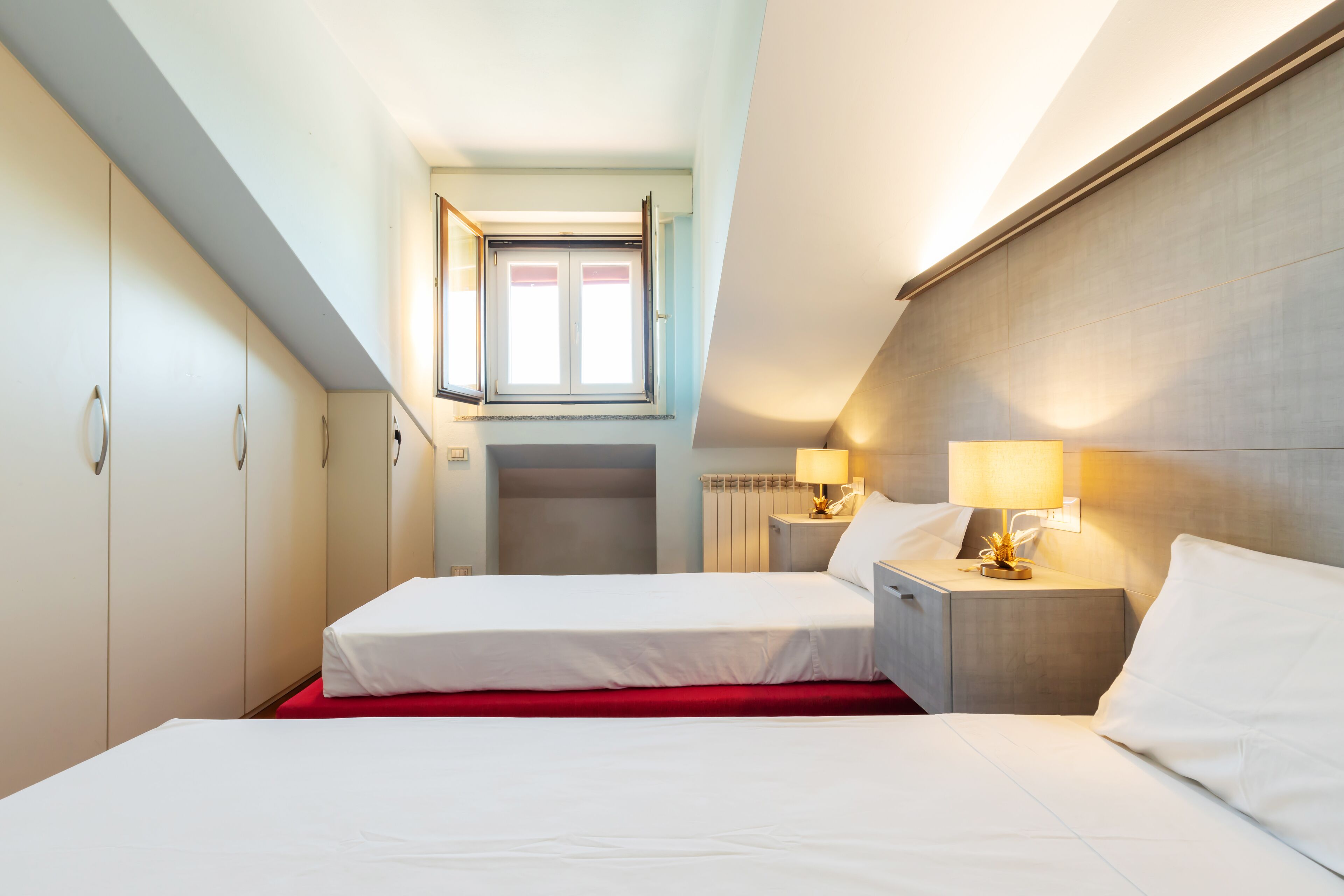 Ein Hotelzimmer mit zwei Betten, einem roten Teppich, einem Fenster mit Jalousien und Nachttischlampen.