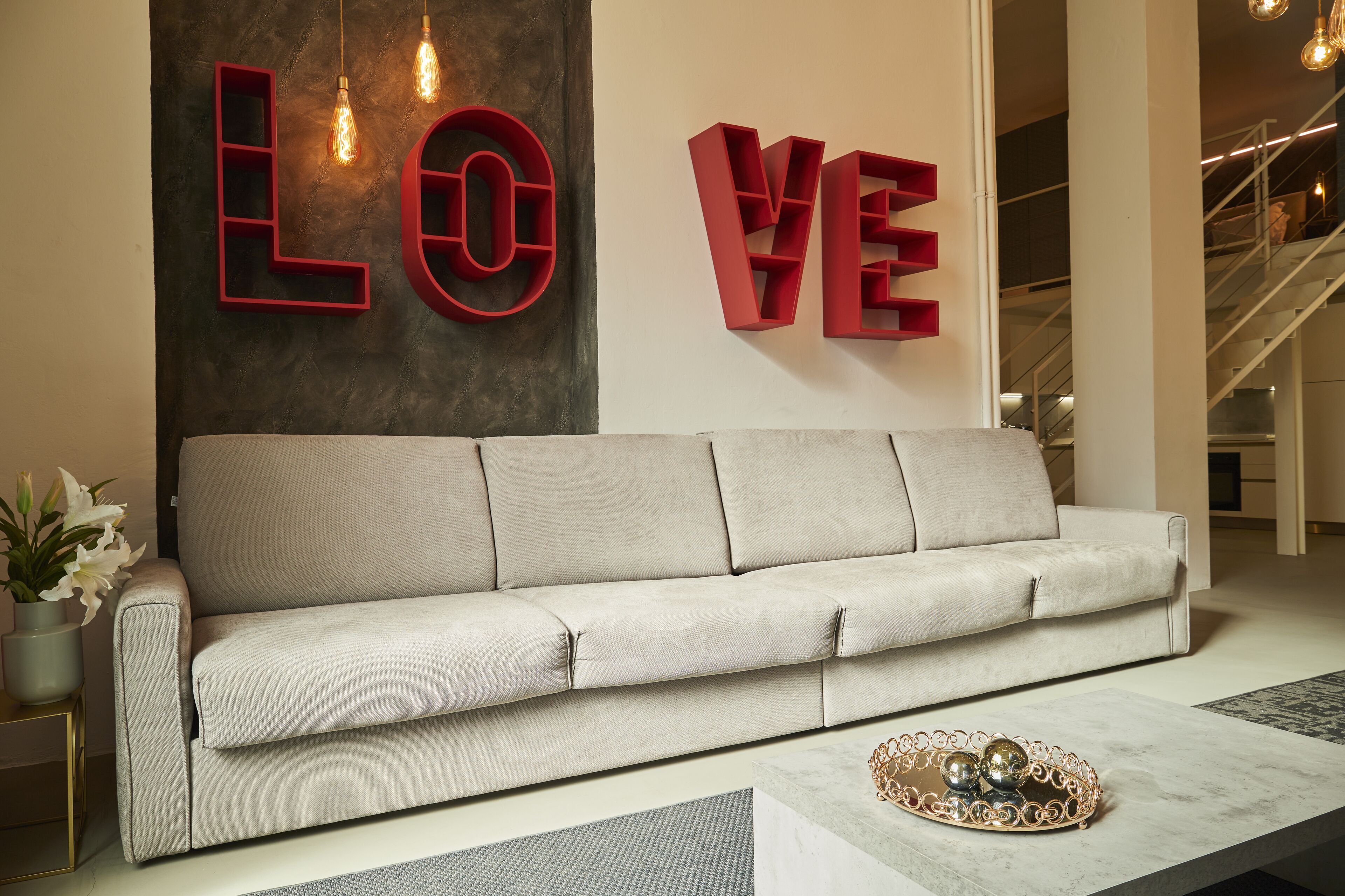 Un salon moderne avec un canapé beige, un mur décoratif orné de lettres formant le mot « AMOUR », et une table basse en marbre agrémentée d’un plateau décoratif.