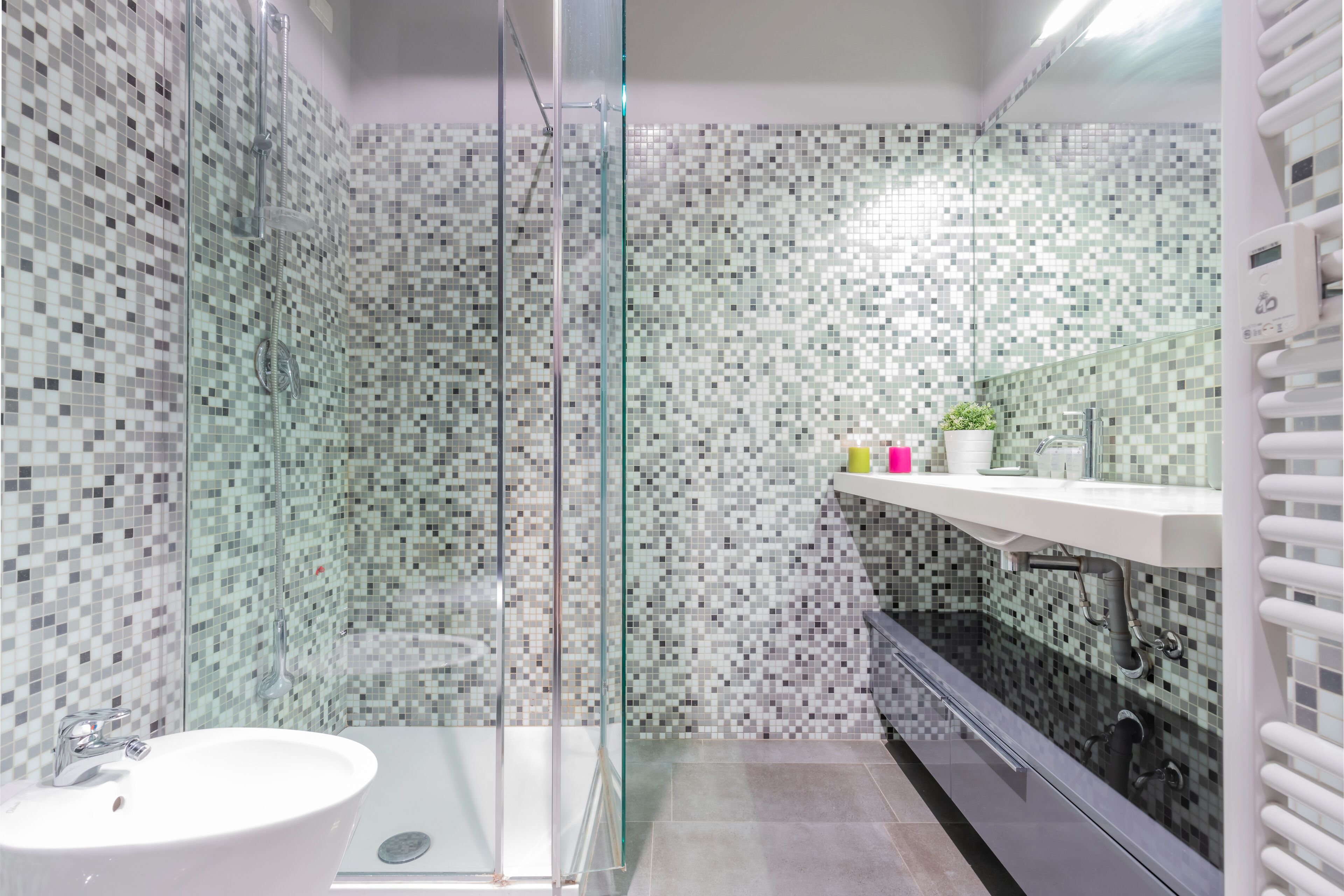 A modern bathroom with a glass shower enclosure, a white sink, and a tiled mosaic backsplash.