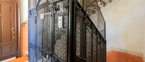 Una escalera con barandillas de metal ornamentadas y una puerta marrón a la izquierda.