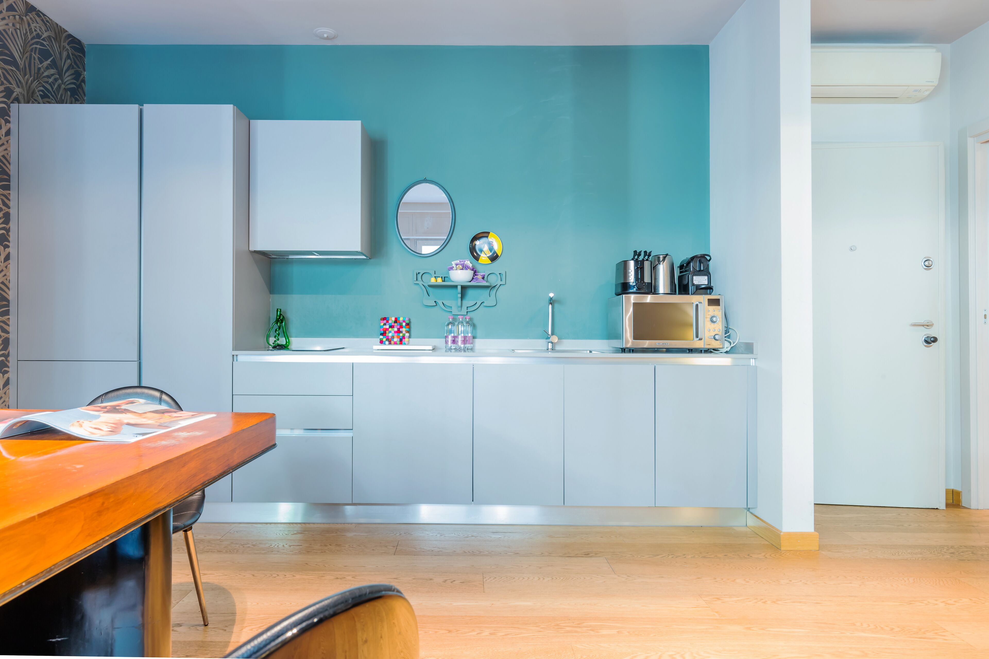 A modern kitchen with white cabinets, a teal backsplash, and a wooden dining table.