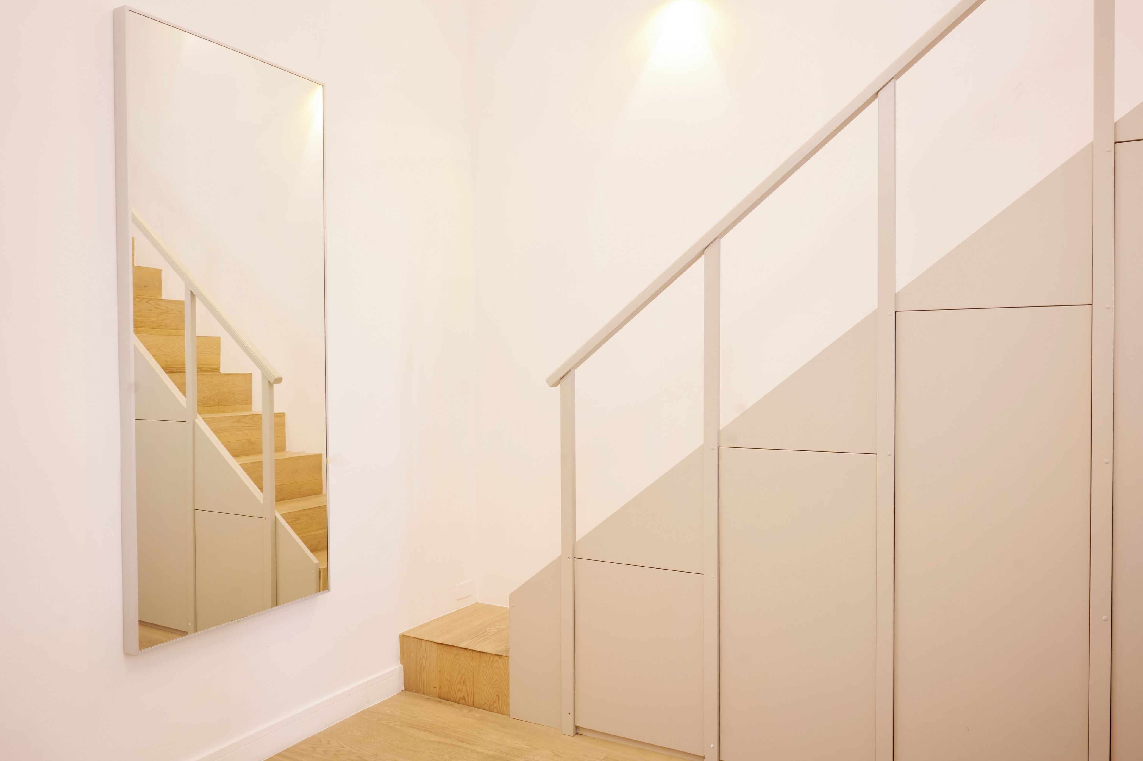 A modern staircase with a wooden finish and a white handrail, leading to a landing with a small wooden platform.
