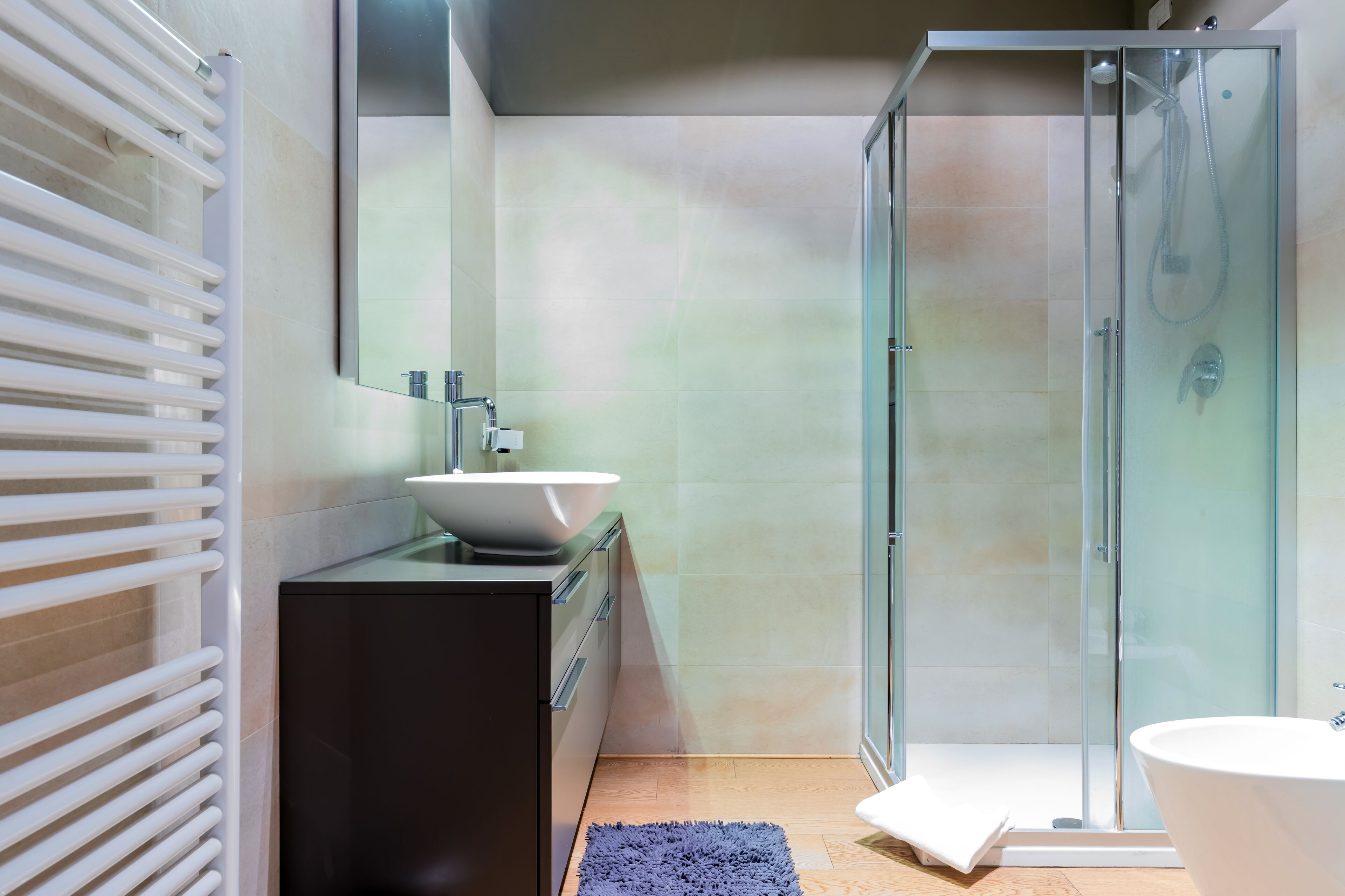 Un bagno moderno con box doccia in vetro, lavandino freestanding e mobile contenitore a incasso.