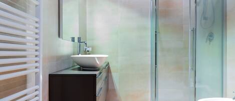 Un bagno moderno con box doccia in vetro, lavandino freestanding e mobile contenitore a incasso.