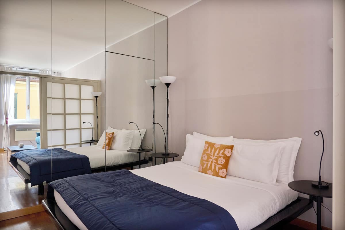 A hotel room with two beds, a large mirror, and a small table with a lamp.