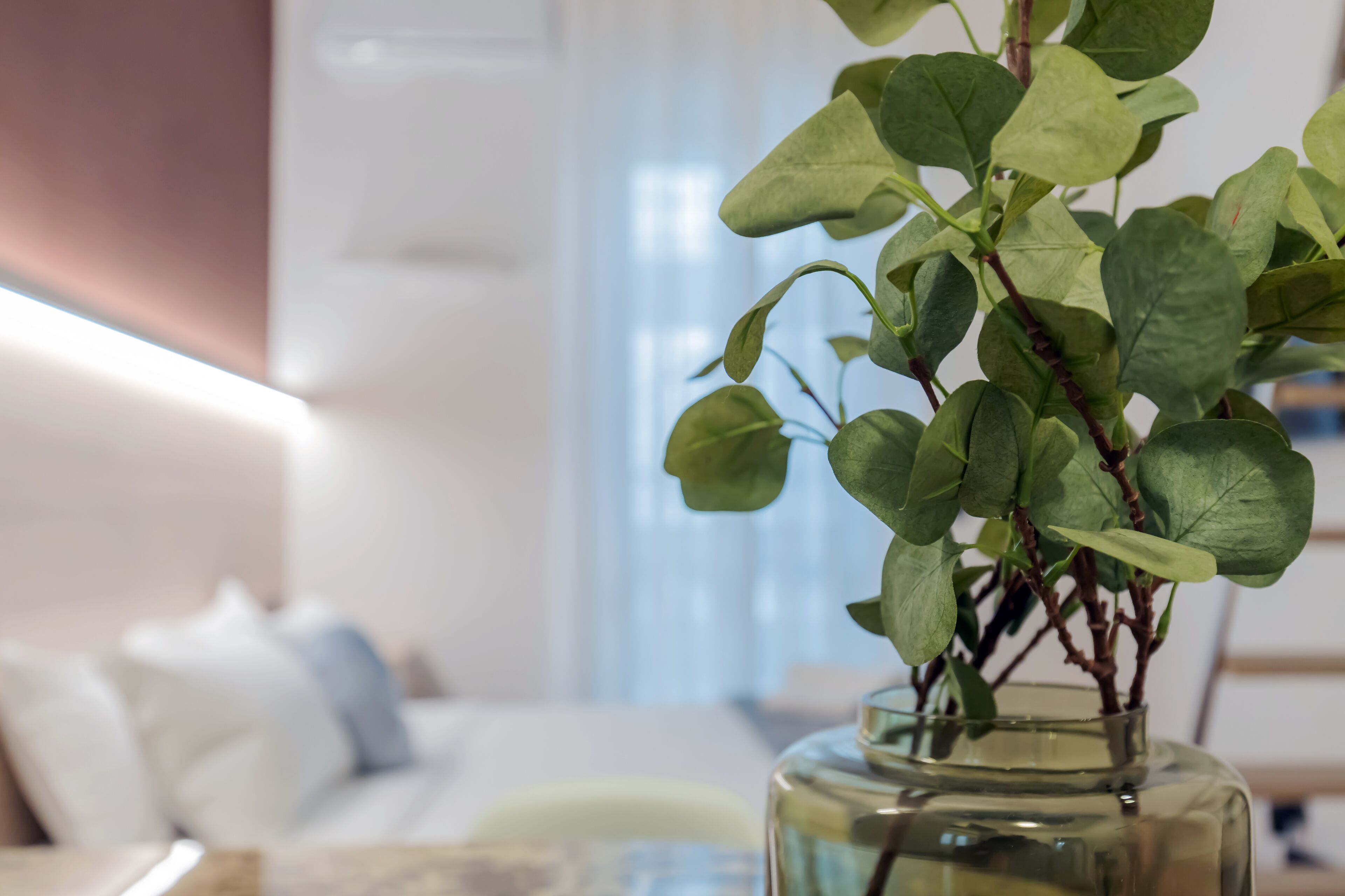 Ein Zimmer mit einem Bett, Kissen und einer Vase mit grünen Blättern zu sehen.