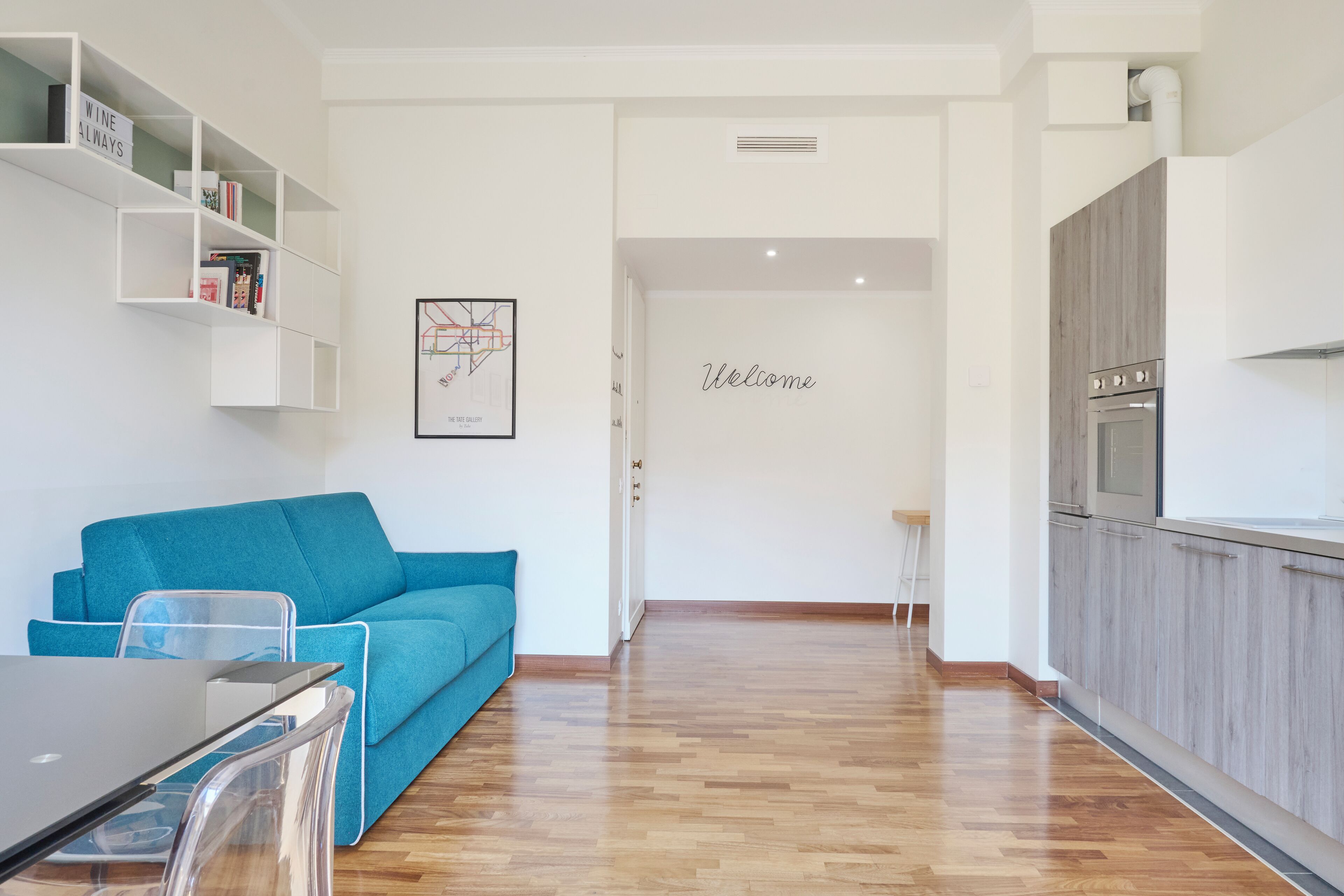A modern living room with a blue sofa, a glass coffee table, and a white bookshelf.