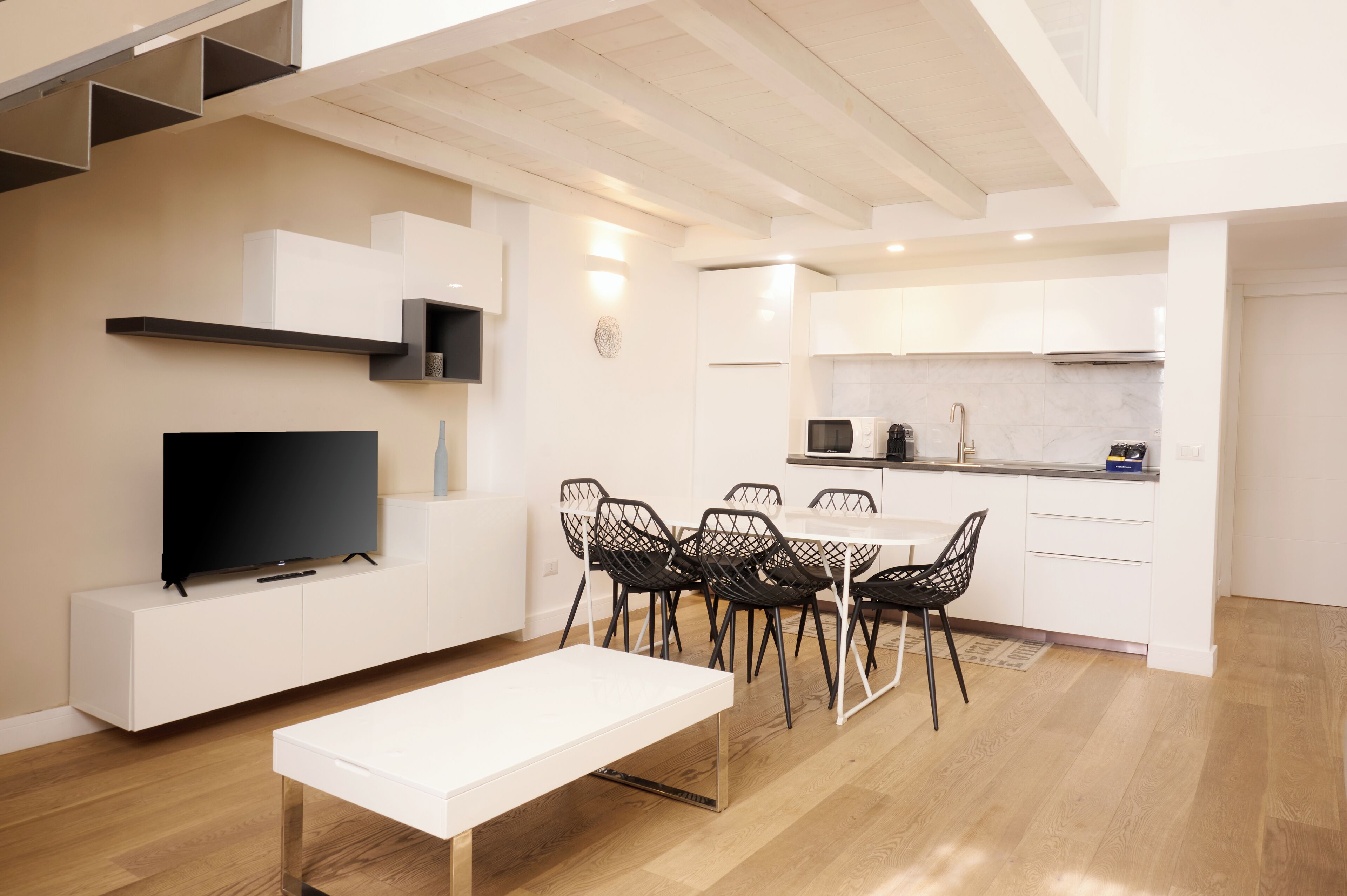 A modern kitchen with white cabinets, a dining area with a white table and black chairs, and a flat-screen TV on a white cabinet.