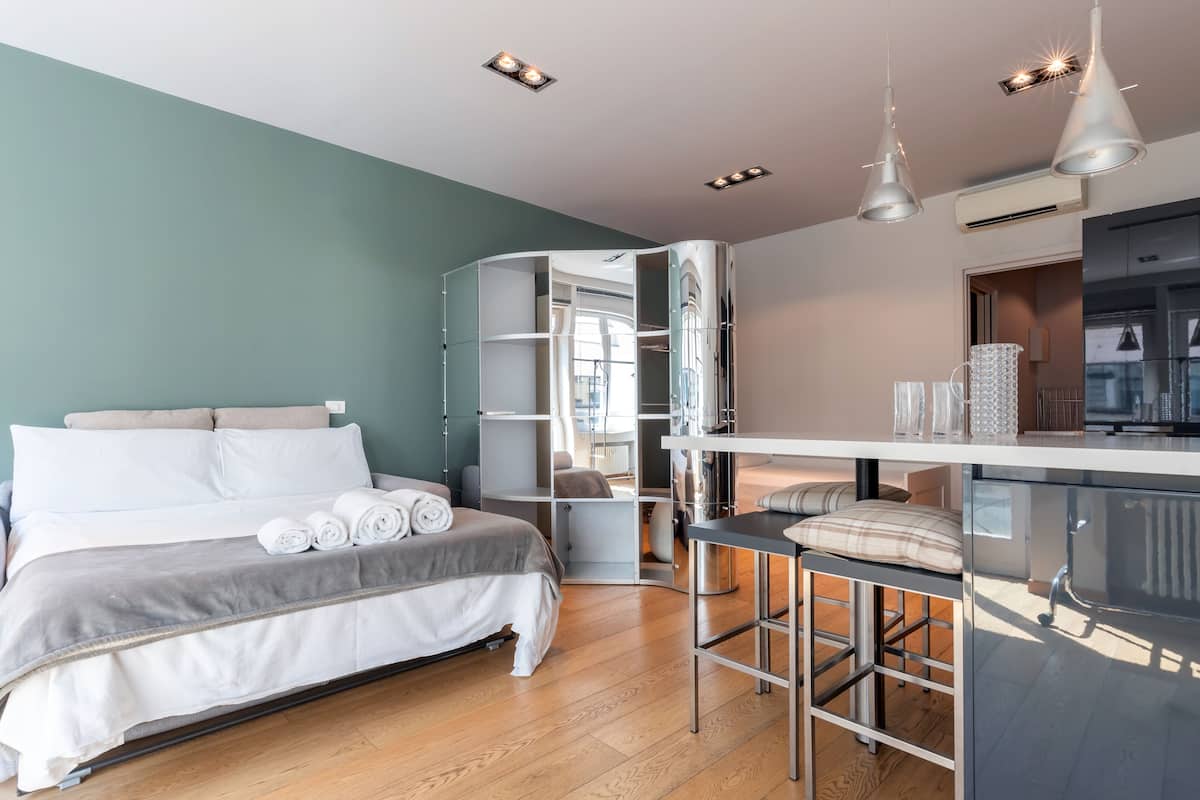 A modern hotel room with a bed, a small kitchenette, and a seating area.