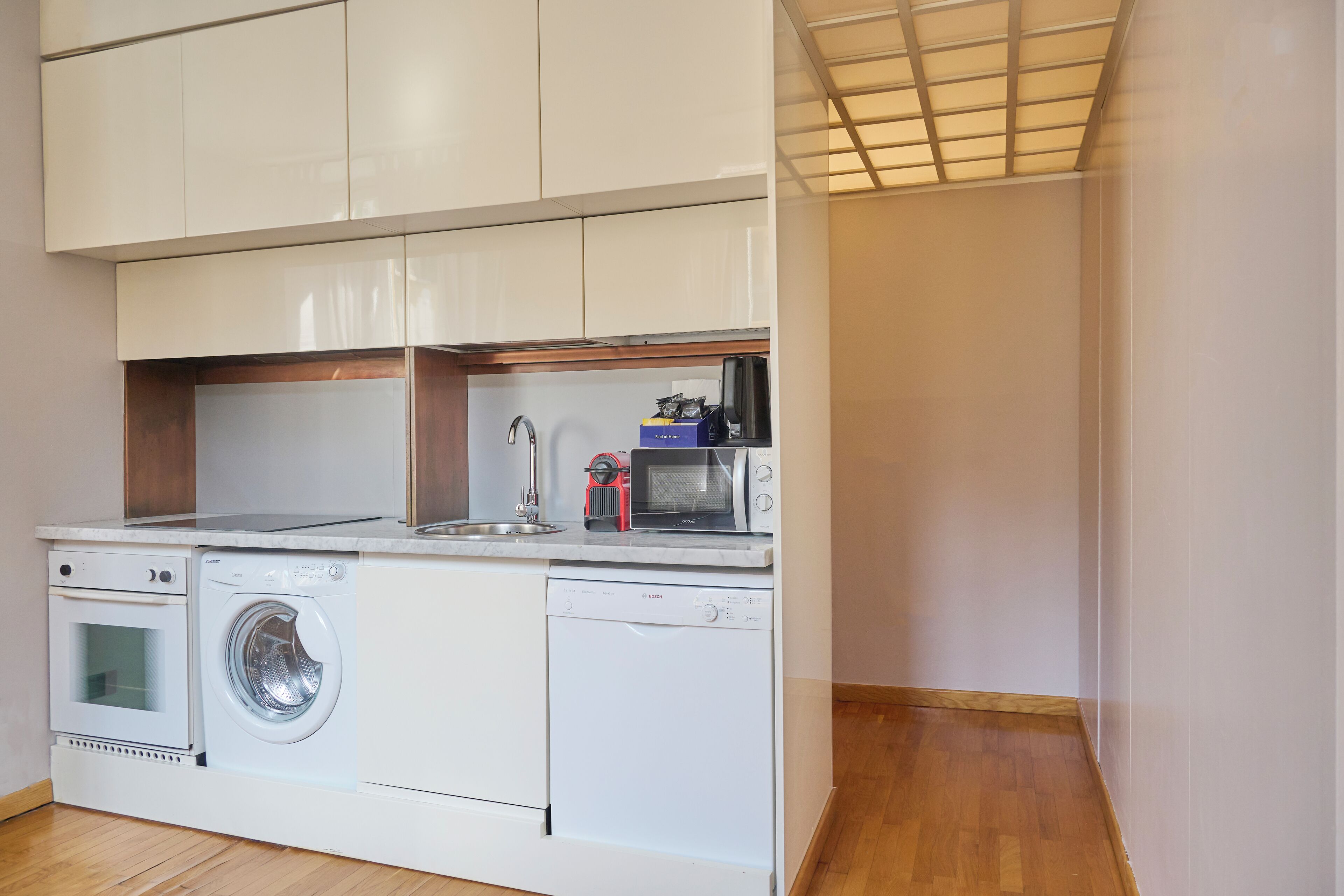 Een compacte keuken met een wasmachine, vaatwasser, magnetron en een klein spoelgedeelte.