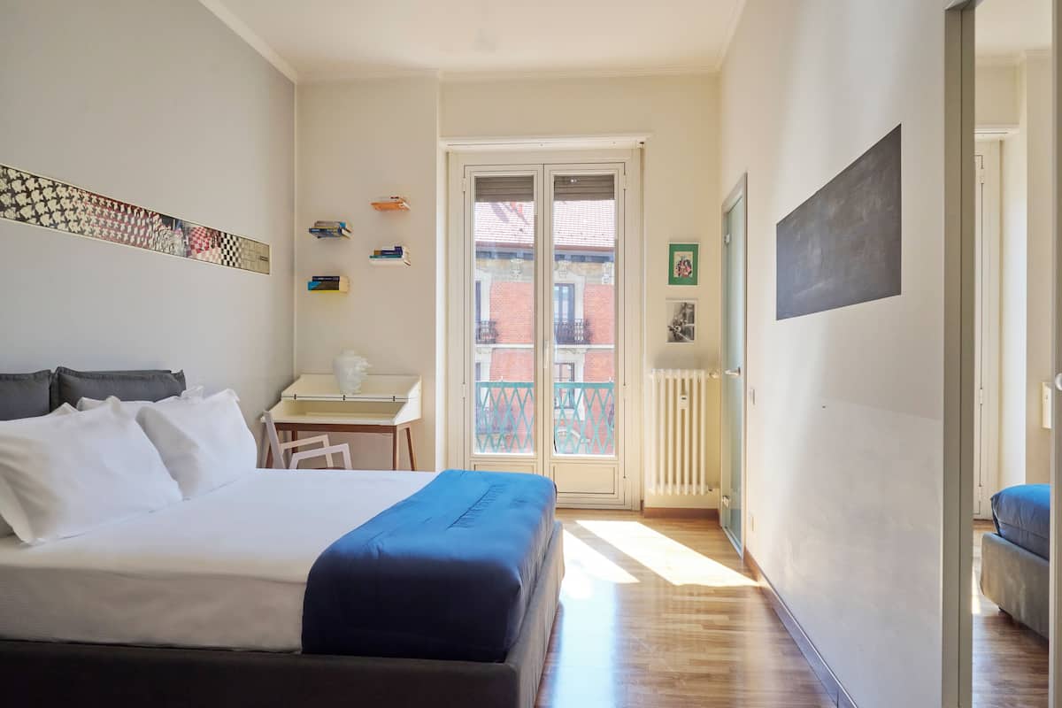 A bedroom with a bed, a desk, and a balcony.