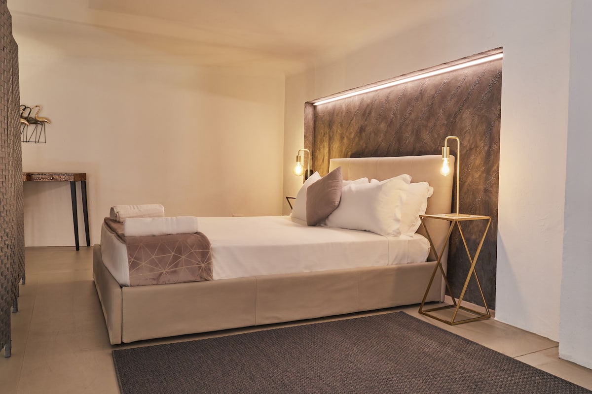 A modern hotel room with a large bed, a bedside table, and a wall-mounted light fixture.