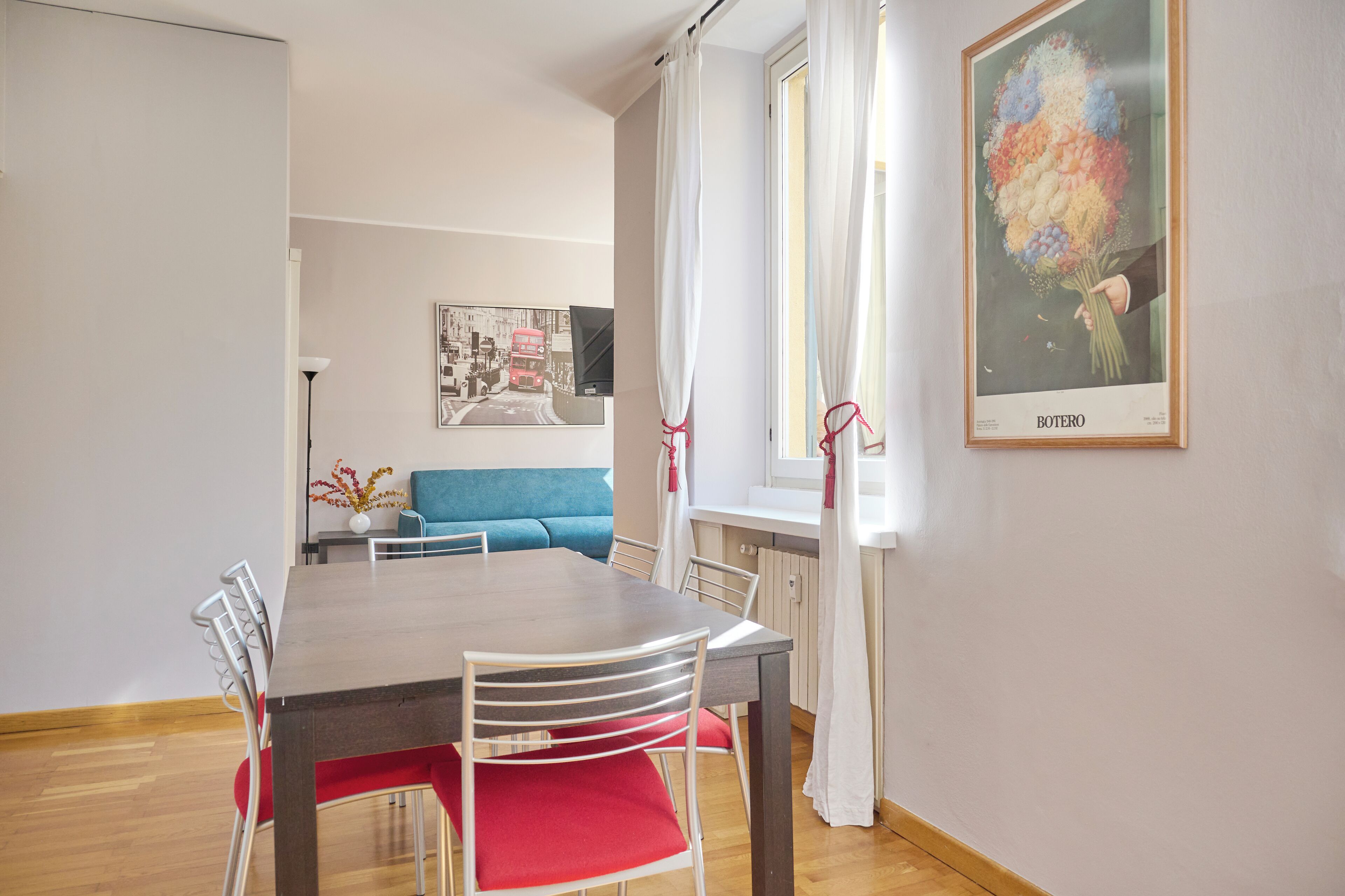 A dining area with a wooden table and chairs, a blue sofa, and a framed picture on the wall.