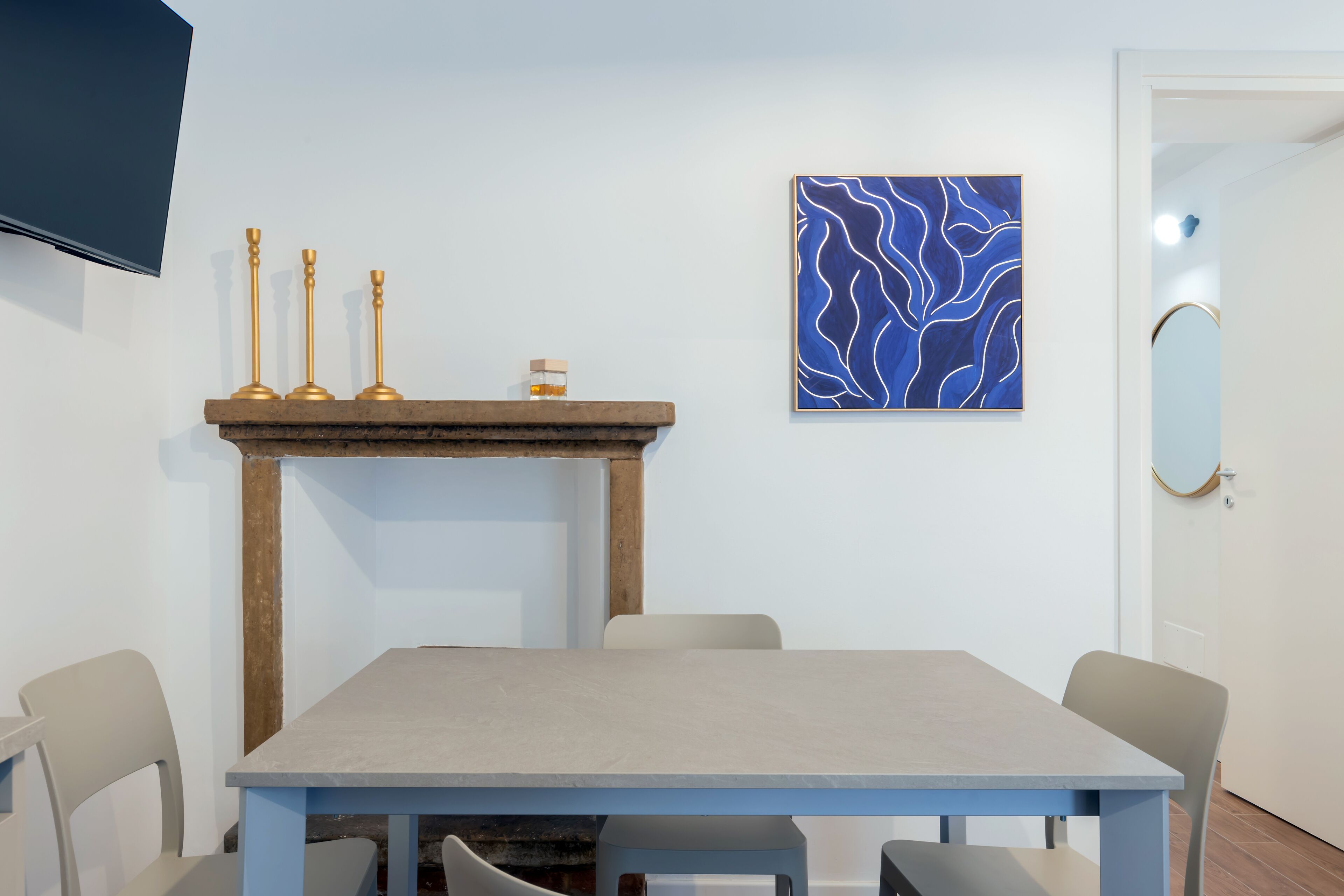 A dining area with a table, chairs, a fireplace, a flat-screen TV, and a wall art piece.