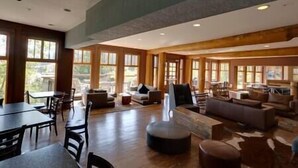 A spacious living area with a high ceiling, large windows, and a mix of seating arrangements including sofas and chairs. - Ski In-Out Location / 1 Bed / Hot Tubs, Pool & Gym (Fernie)