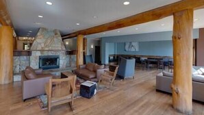 A spacious living area with a stone fireplace, wooden beams, and modern furniture. - Ski In-Out Location / 1 Bed / Hot Tubs, Pool & Gym (Fernie)