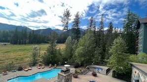 A pool area with two pools, surrounded by trees and a mountain backdrop. - Ski In-Out Location / 1 Bed / Hot Tubs, Pool & Gym (Fernie)