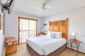 A bedroom with a bed, a wooden headboard, a ceiling fan, a small wooden table, a nightstand, and a window with blinds. - Ski In-Out Location / 1 Bed / Hot Tubs, Pool & Gym (Fernie)
