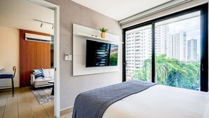 Ett modernt hotellrum med en stor säng, en tv som är monterad på väggen, en liten sittgrupp med en soffa och en fåtölj samt en balkong med utsikt över staden.
