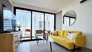 A modern living room with a yellow sofa, a round mirror, and a view of tall buildings through large windows. - w* | High-end 1BR in San Francisco w/ Balcony (Panamá)