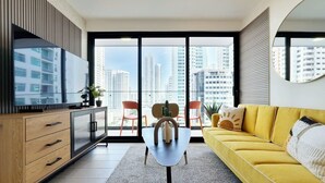 A modern living room with a yellow sofa, a wooden cabinet, a glass-top coffee table, and a large window offering a city view. - w* | High-end 1BR in San Francisco w/ Balcony (Panamá)