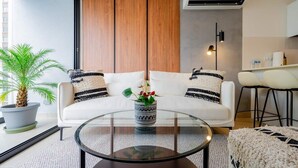 Ein modernes Wohnzimmer mit einem weißen Sofa, einem Glastisch und einer Topfpflanze.