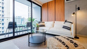 Ein modernes Wohnzimmer mit einem weißen Sofa, einem runden Couchtisch und einem großen Fenster mit Blick auf die Stadt.