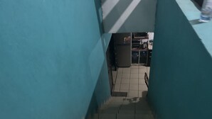 Un pasillo estrecho con suelo de baldosas que conduce a una habitación con suelo de cerámica y una cocina visible, con refrigerador y pileta.