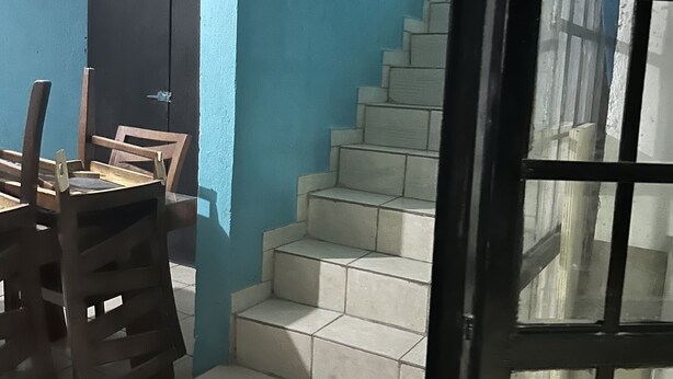 Una habitación con pared azul, una mesa de comedor de madera con sillas, una escalera y una puerta con paneles de vidrio.