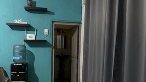 Una habitación con paredes color turquesa, un dispensador de agua, una silla, una mesa, un frasco de desinfectante para manos y una cortina.