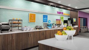 A modern breakfast area with a counter displaying pastries, a bowl of fruit, and a sign for 'Top It Breakfast'. - Tru by Hilton Jacksonville West I 295 (Jacksonville)