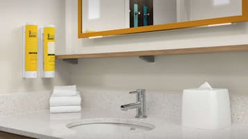 Une salle de bain avec un lavabo blanc, un miroir et deux distributeurs de savon jaunes.