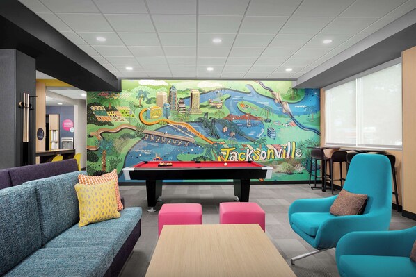 Una mesa de billar en una habitación con un mural colorido, un sofá azul y un sillón color turquesa.